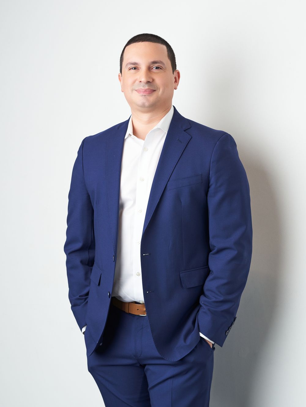 Professional in a navy blue suit and white shirt poses confidently against white background.
