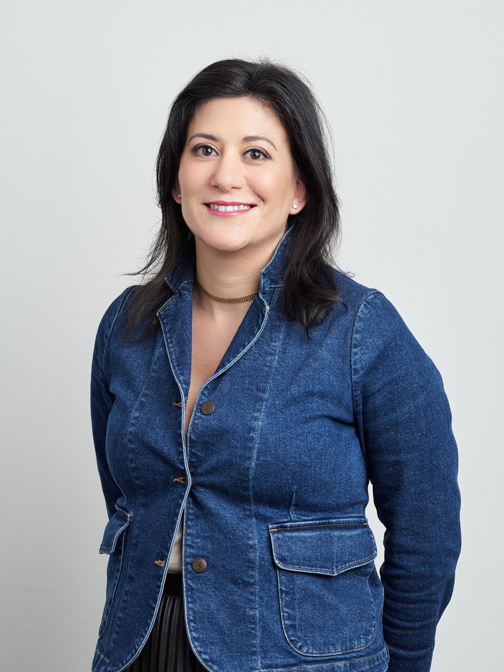 Woman in denim jacket poses confidently against white studio backdrop in casual fashion series.