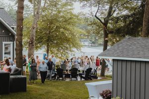 Lakeside wedding venue with gray buildings and white tents surrounded by trees.
