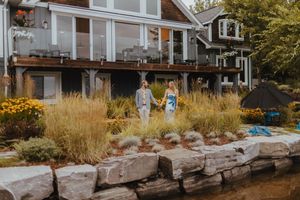 A couple walks along a landscaped stone path with waterfront houses in the background.