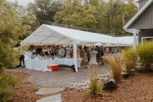 Outdoor wedding setup with white tent canopies and natural landscaping on gravel ground.
