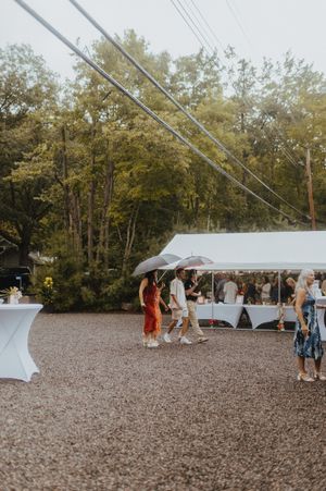 Wedding guests gathering under white tent canopies on a gravel venue space.