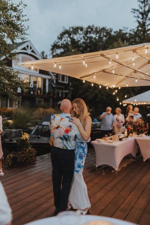 A couple dances under string lights at an outdoor wedding reception on a wooden deck.