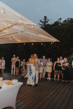 Wedding guests gather on a deck under a canopy with string lights during an evening celebration.
