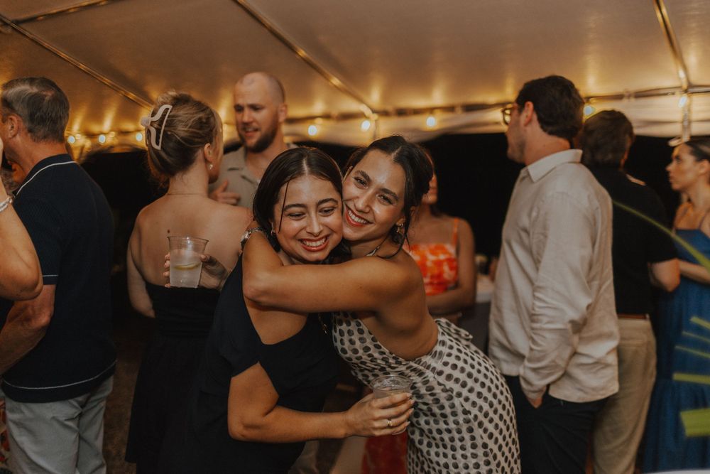 Wedding guests embrace and celebrate on a dance floor under warm tent lighting.