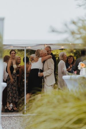 Wedding celebration under white tent with guests mingling in formal attire.