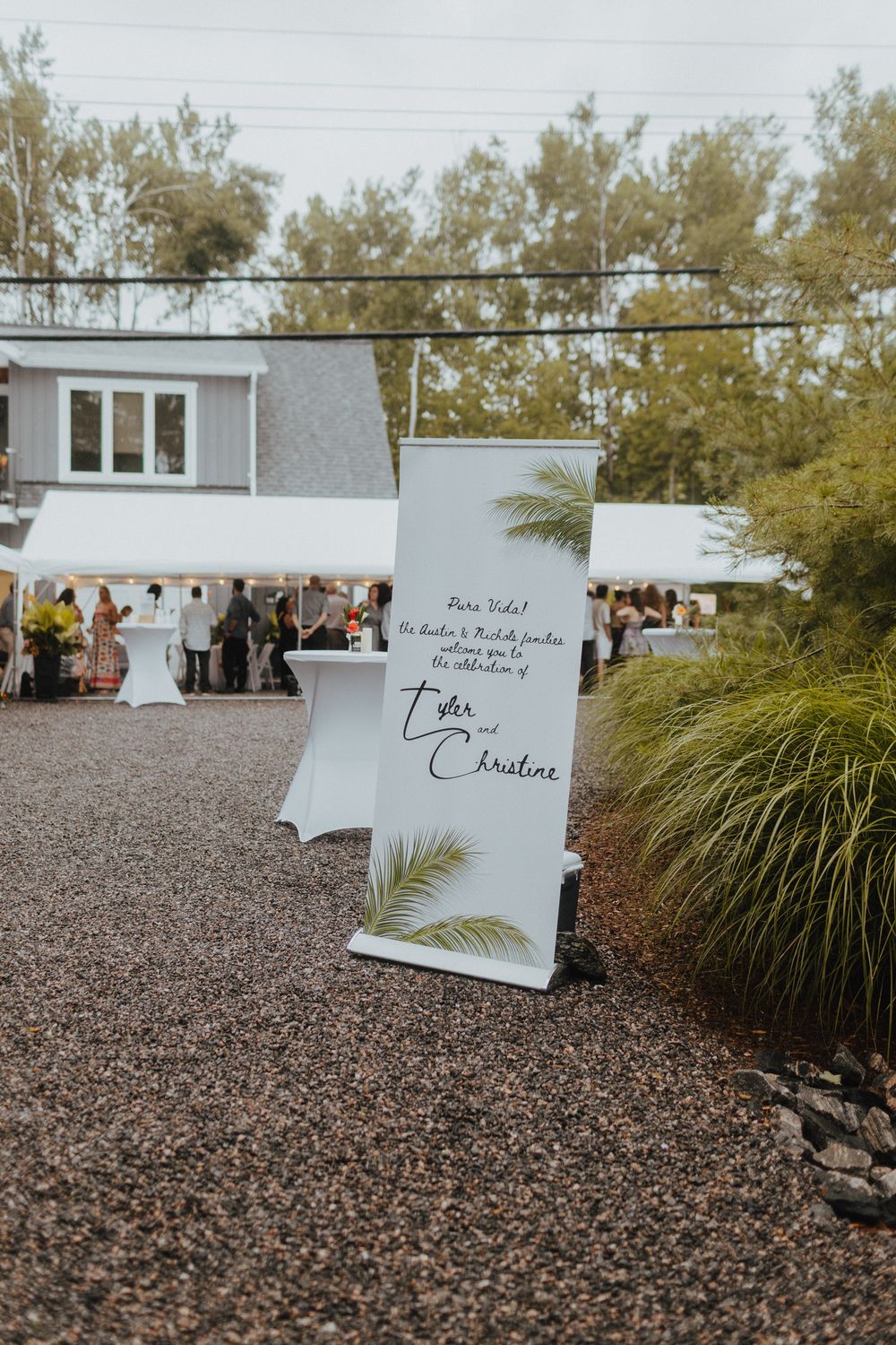 White wedding signage displayed on gravel ground with ornamental grasses in the background.