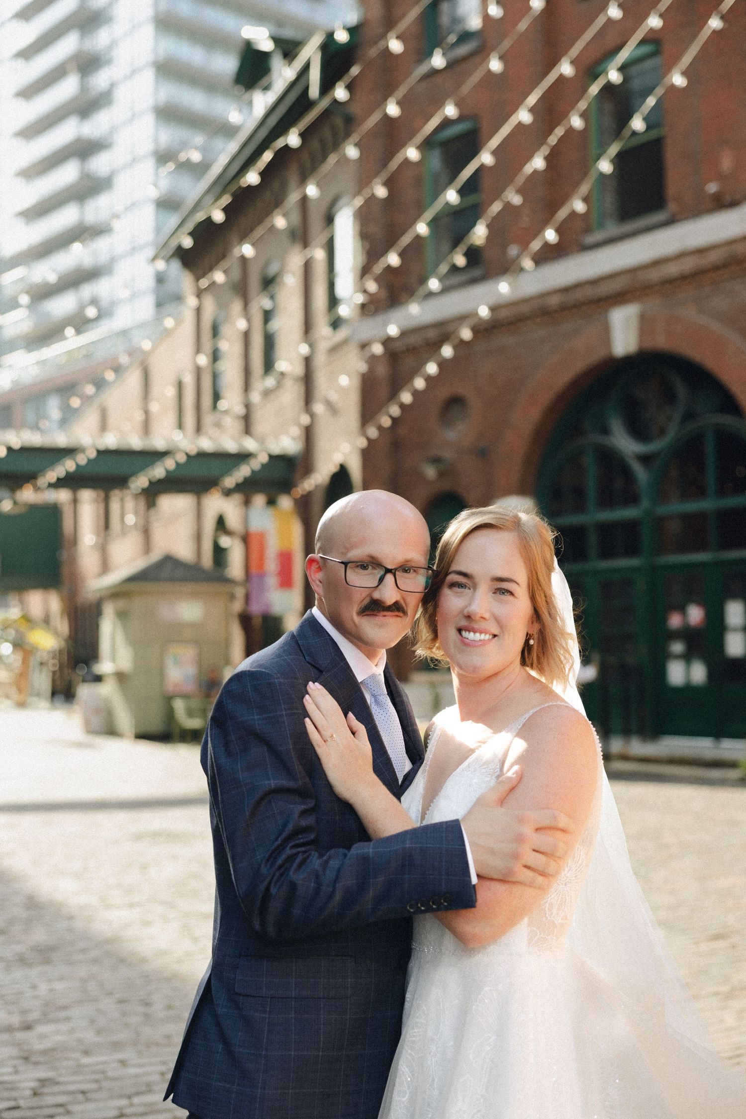 A wedding couple poses in front of historic brick buildings with green doors and windows during their special day.