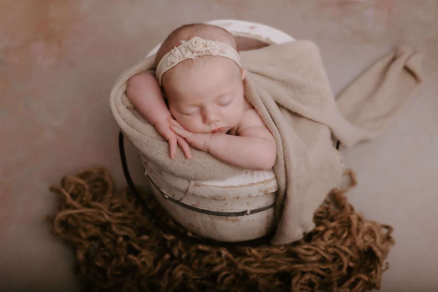A sleeping newborn baby wrapped in soft beige fabric rests peacefully in a round woven basket.