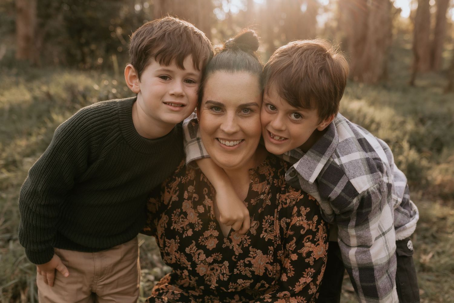 A family poses together outdoors during golden hour in a natural setting wearing casual clothing.