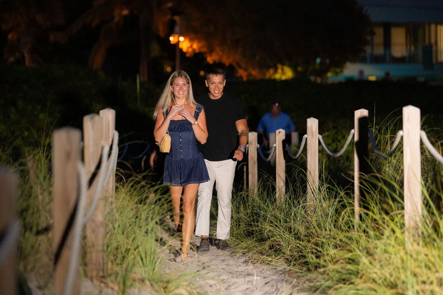 Beach proposal scene showing couples silhouetted against illuminated marquee letters at sunset.