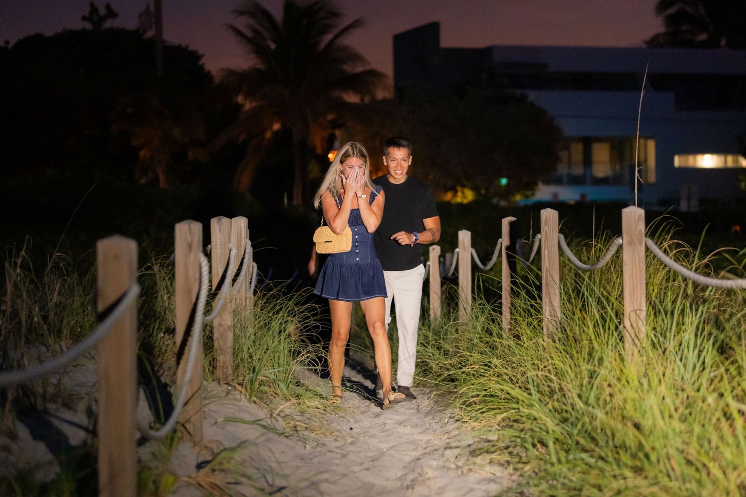 People walk along a scenic beach boardwalk path lined with wooden posts at dusk.