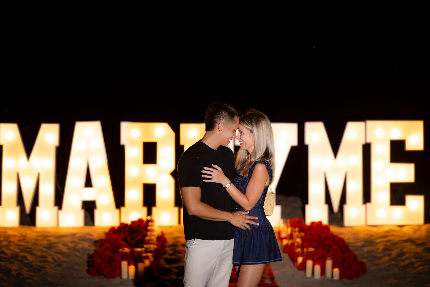 Dancing couple embraces near illuminated lettering at an evening event venue.