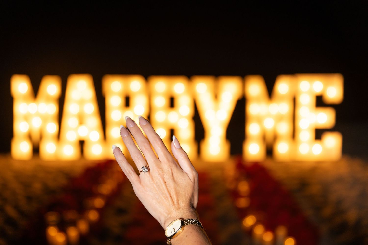 A ring sparkles in front of illuminated 'MARRY ME' letters during nighttime marriage proposal setup.