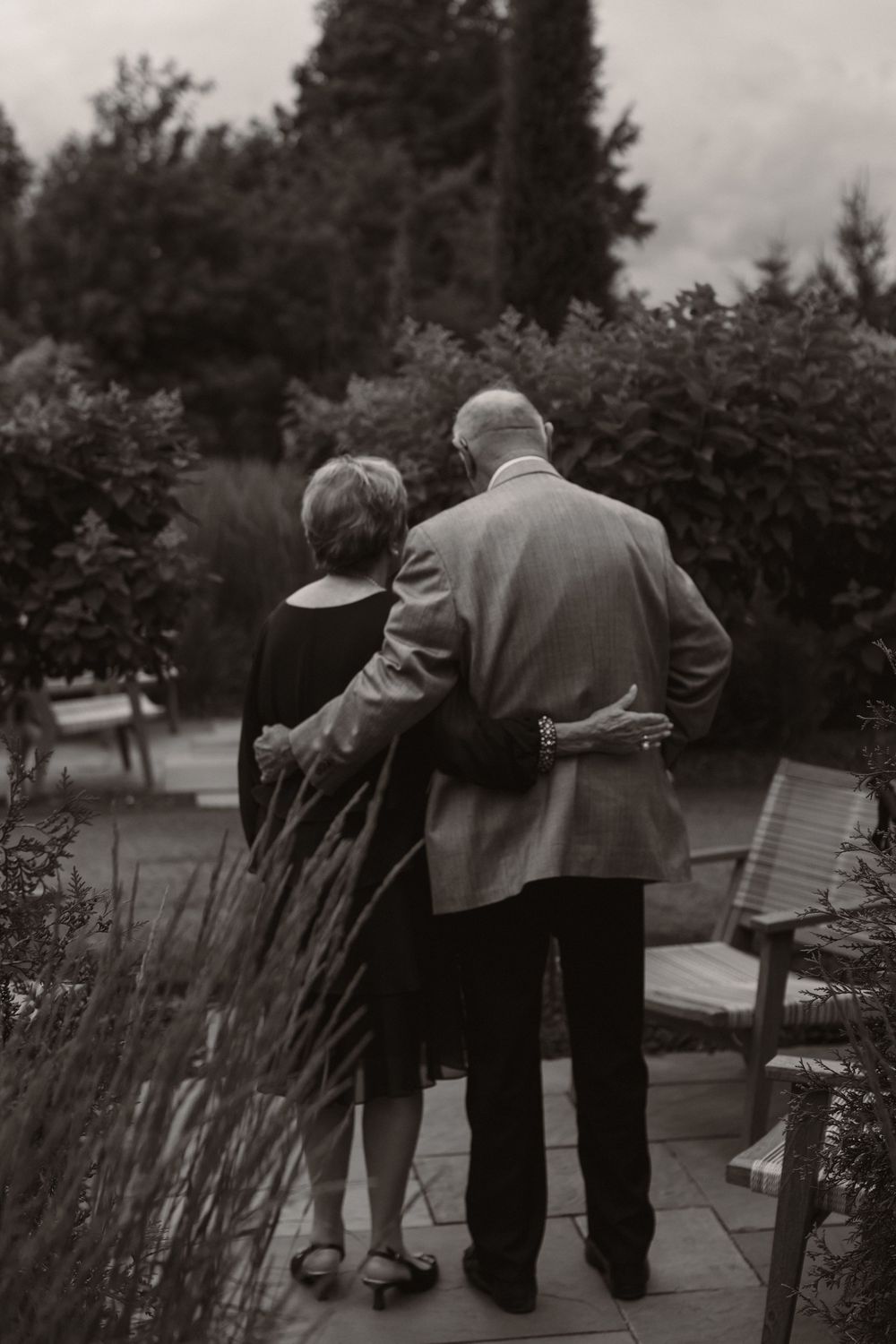 Black and white photo of wedding guests gathered along garden path at outdoor venue.