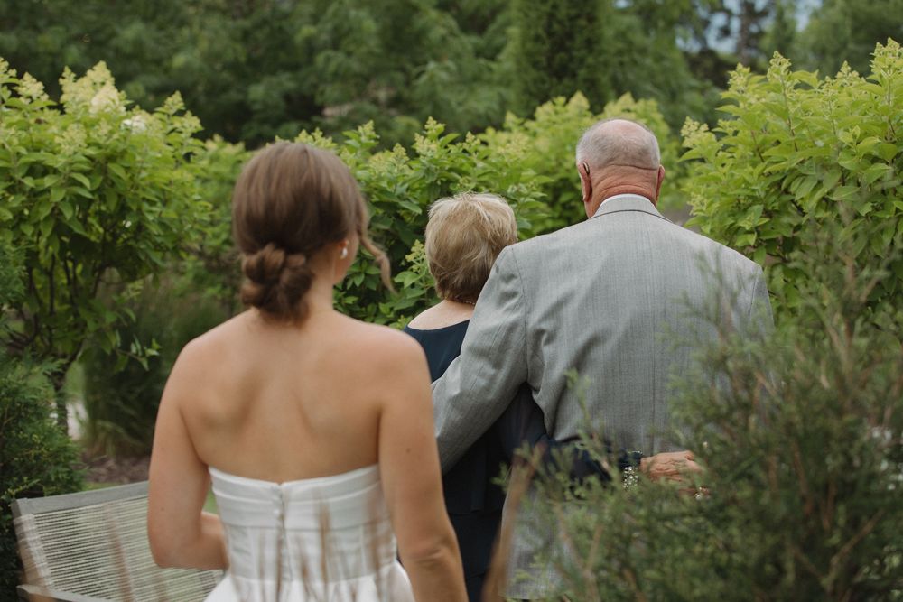 Wedding party members walking through lush garden setting during summer celebration.
