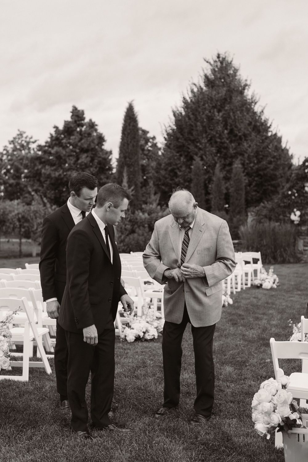 Wedding party members examining decorative white chairs set up for outdoor ceremony.