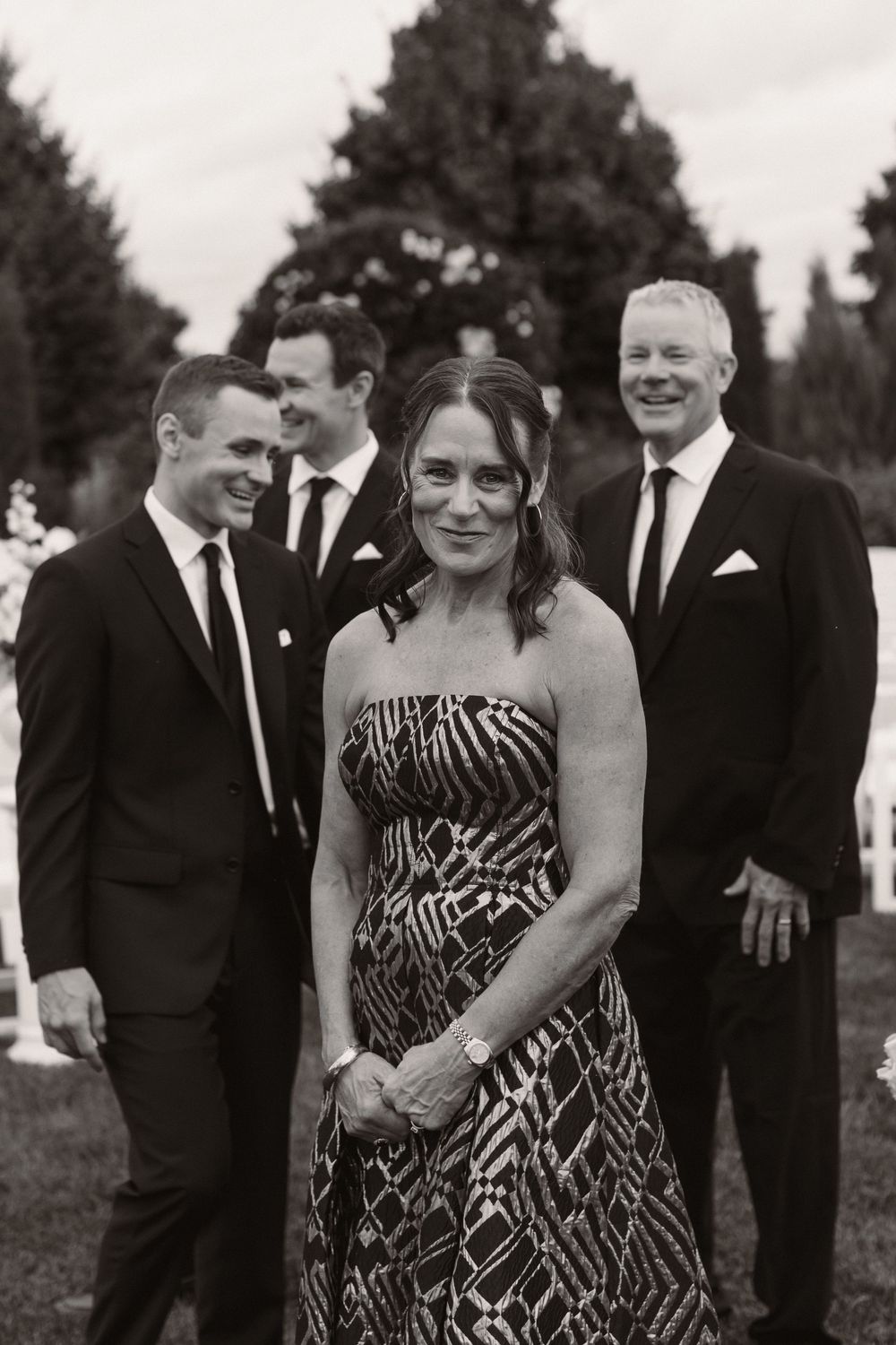 Wedding party members in formal attire pose together outdoors in black and white photography.