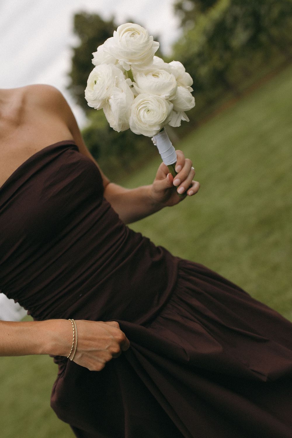 Close-up of white rose bouquet held against brown bridesmaid dress outdoors.