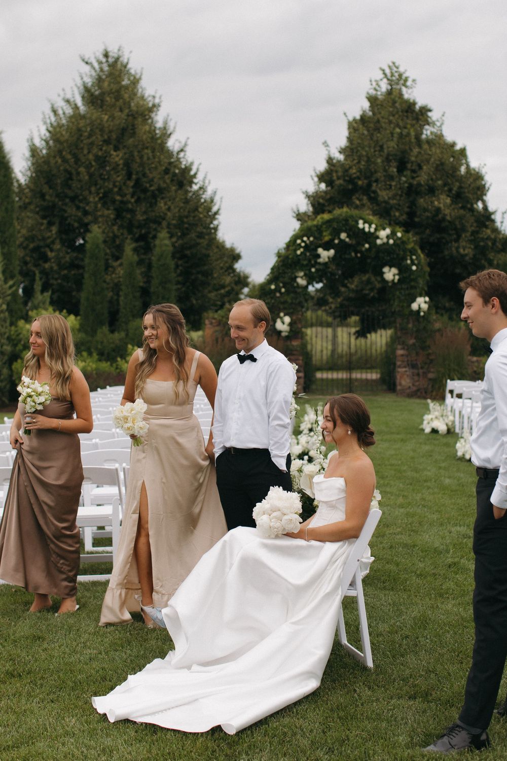 Wedding ceremony setup on lawn with white chairs and floral arch.