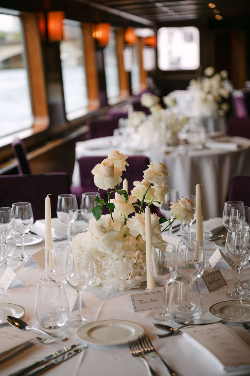 Elegant wedding reception table set with white floral centerpieces and formal place settings.