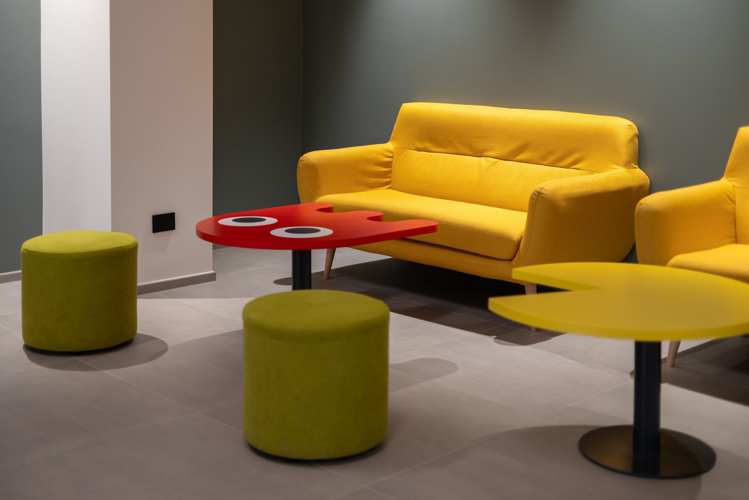 Contemporary office lounge features vibrant yellow sofas and green ottoman seating arranged around modern black tables.
