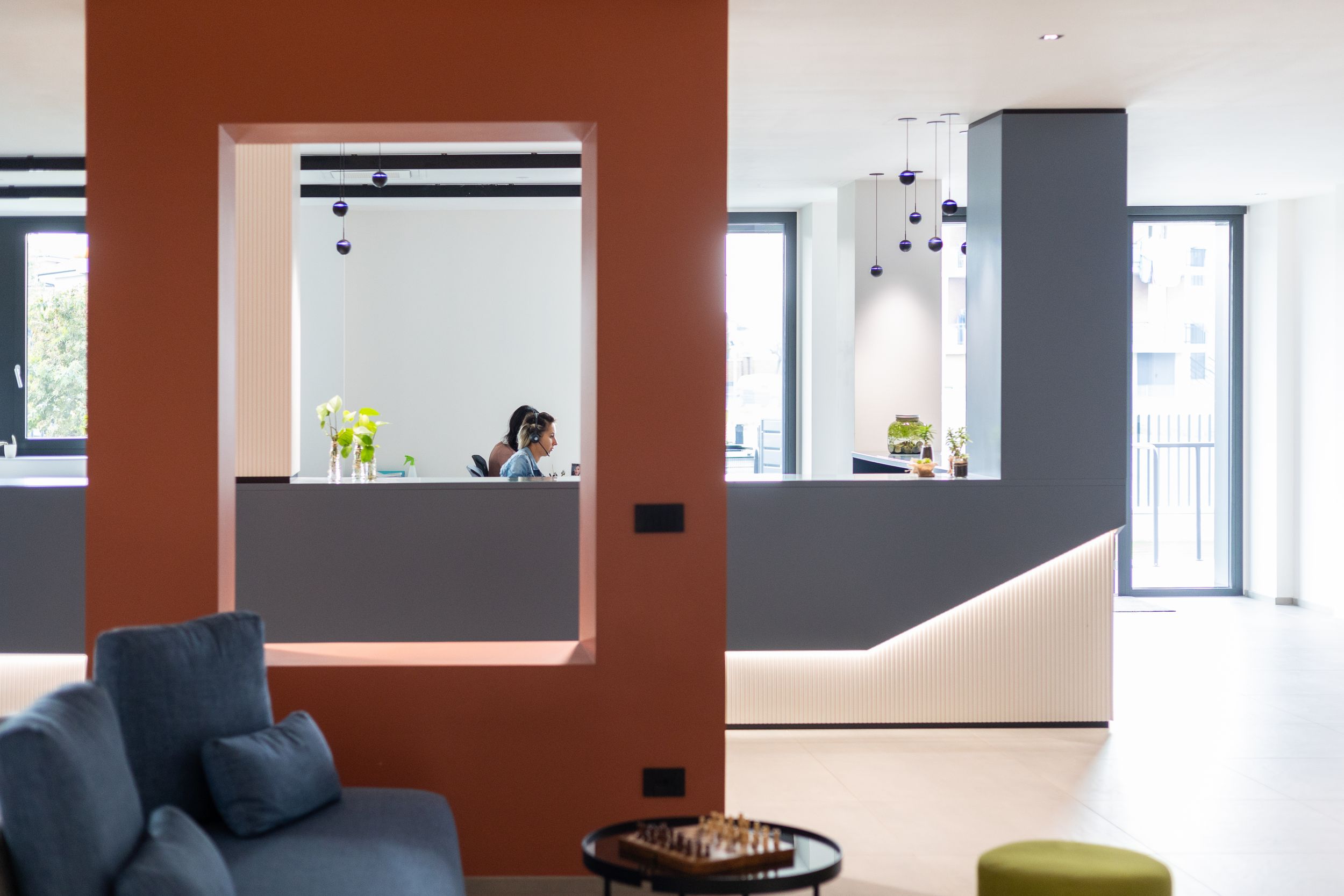 Modern open office space with orange accent walls, glass partitions, and contemporary lighting fixtures.
