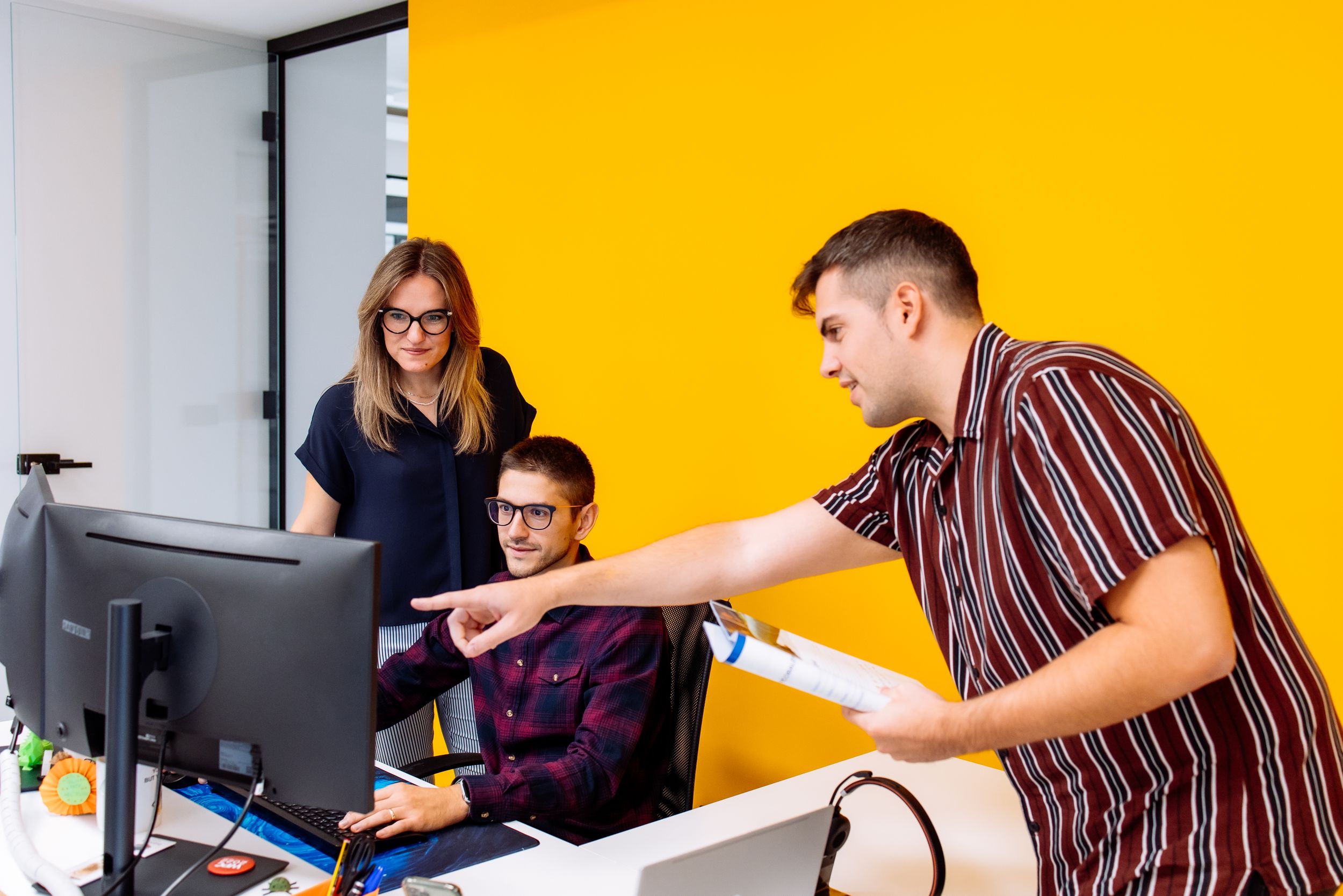 People working in a modern office environment with bright yellow walls while looking at computer screens together.