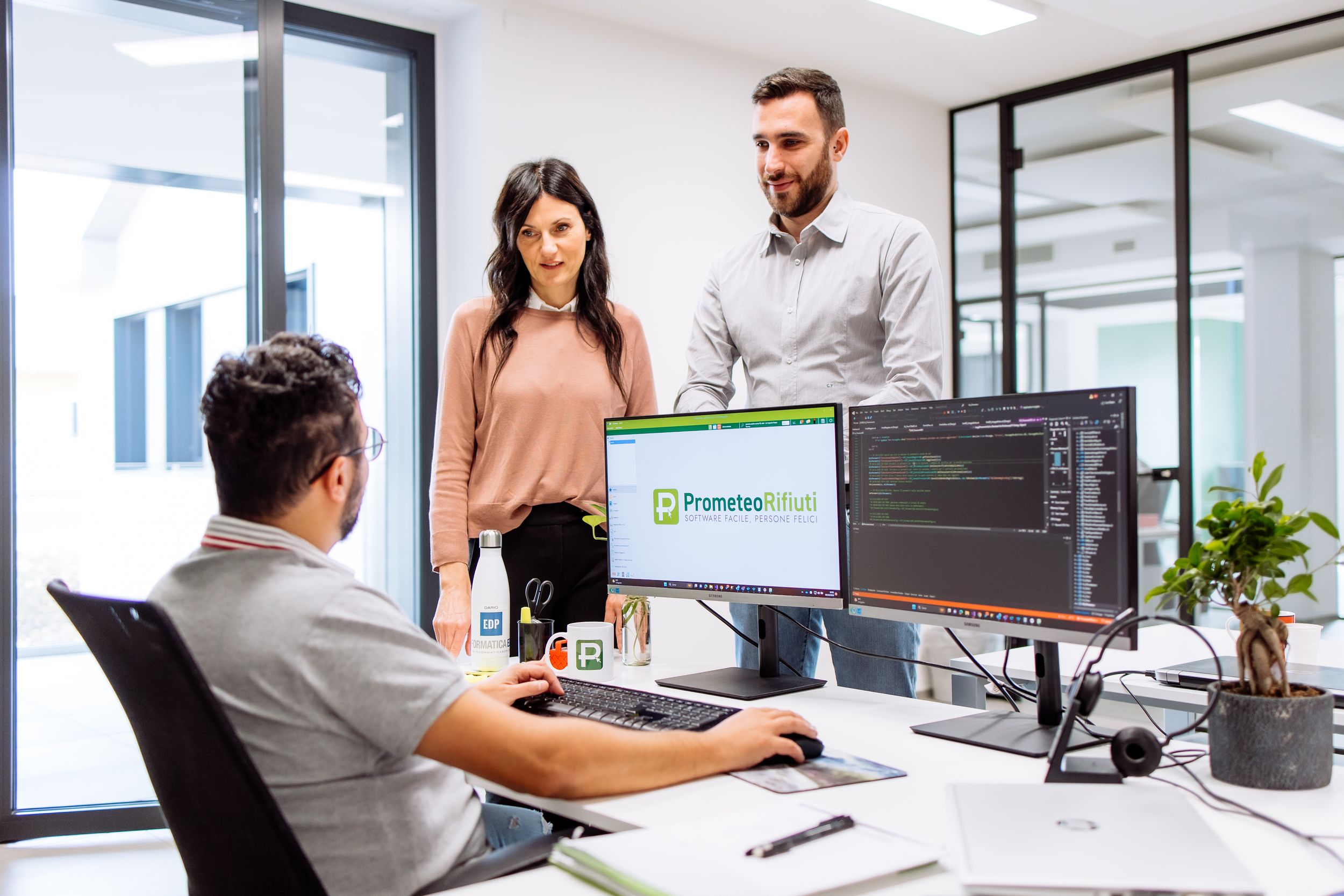 Business professionals working together in a modern open office space with computers and collaborative workstations.
