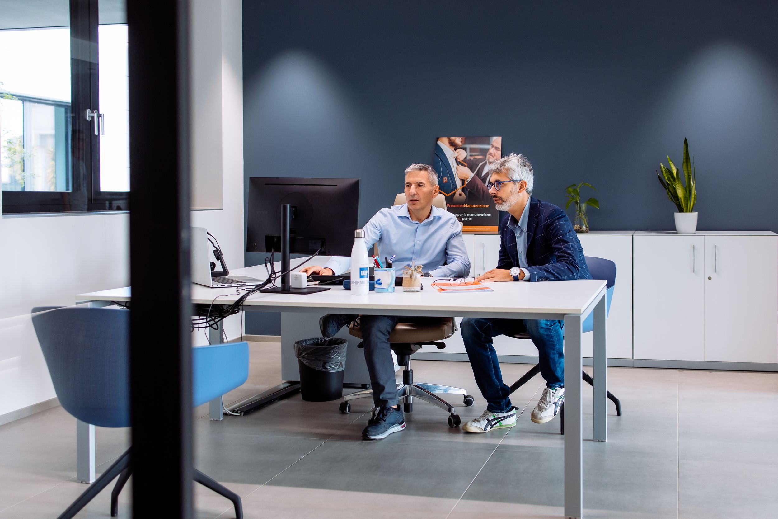 Business colleagues meet in modern office meeting room with glass walls and natural lighting.