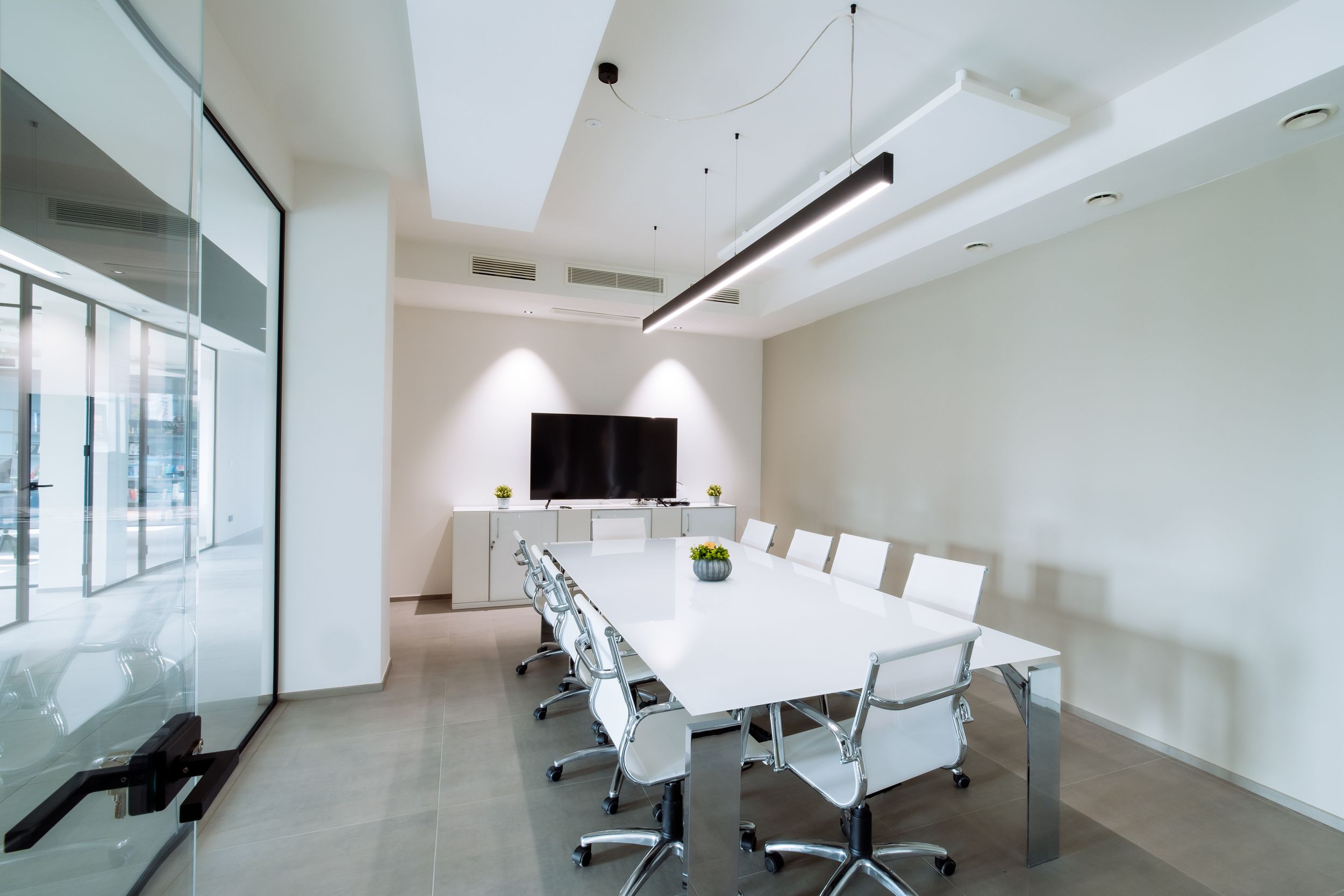 Modern office interior with clean white walls, glass partitions, and minimalist furniture in an open workspace layout.