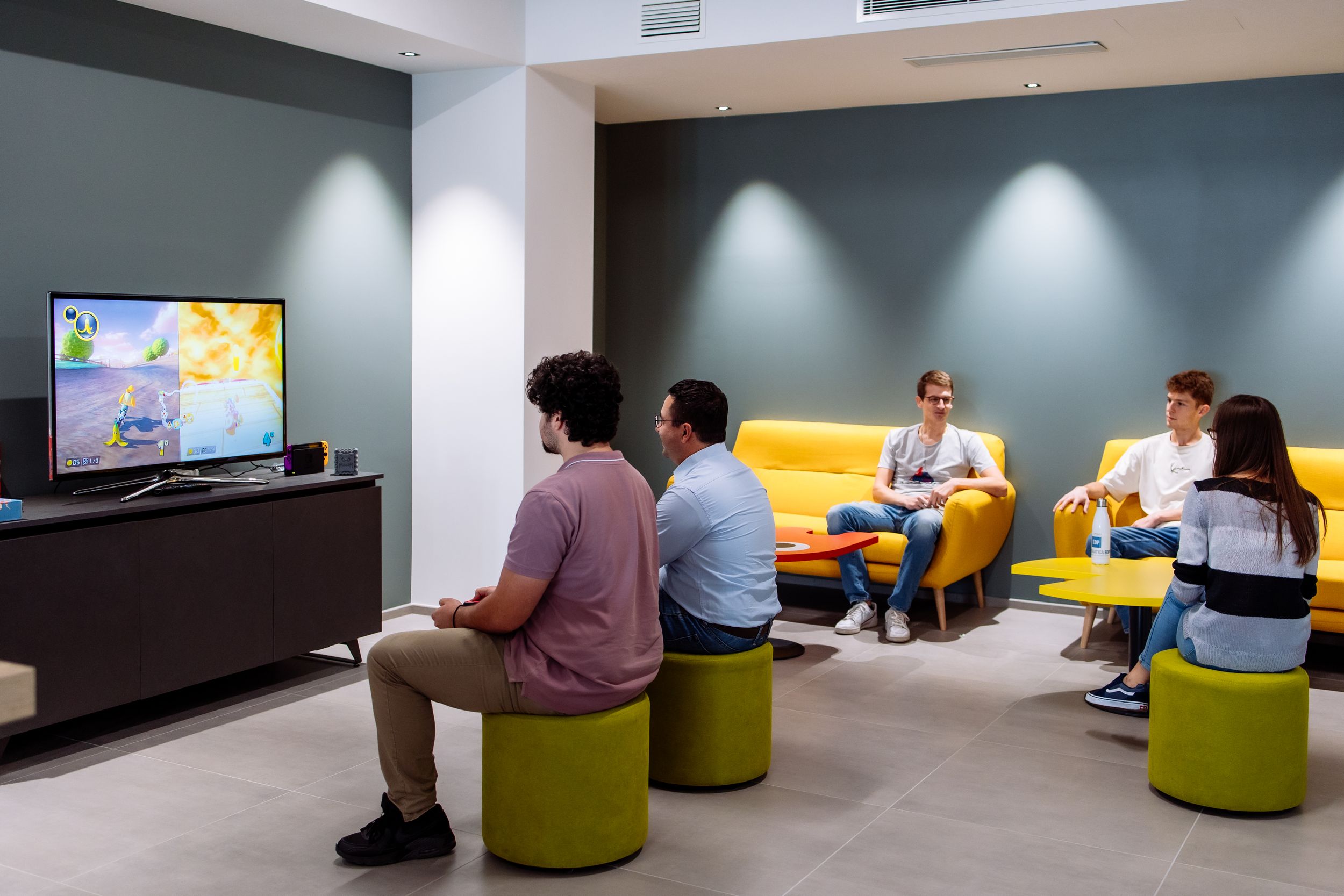 Casual meeting area with colorful ottomans and TV screen for collaborative workspace sessions.