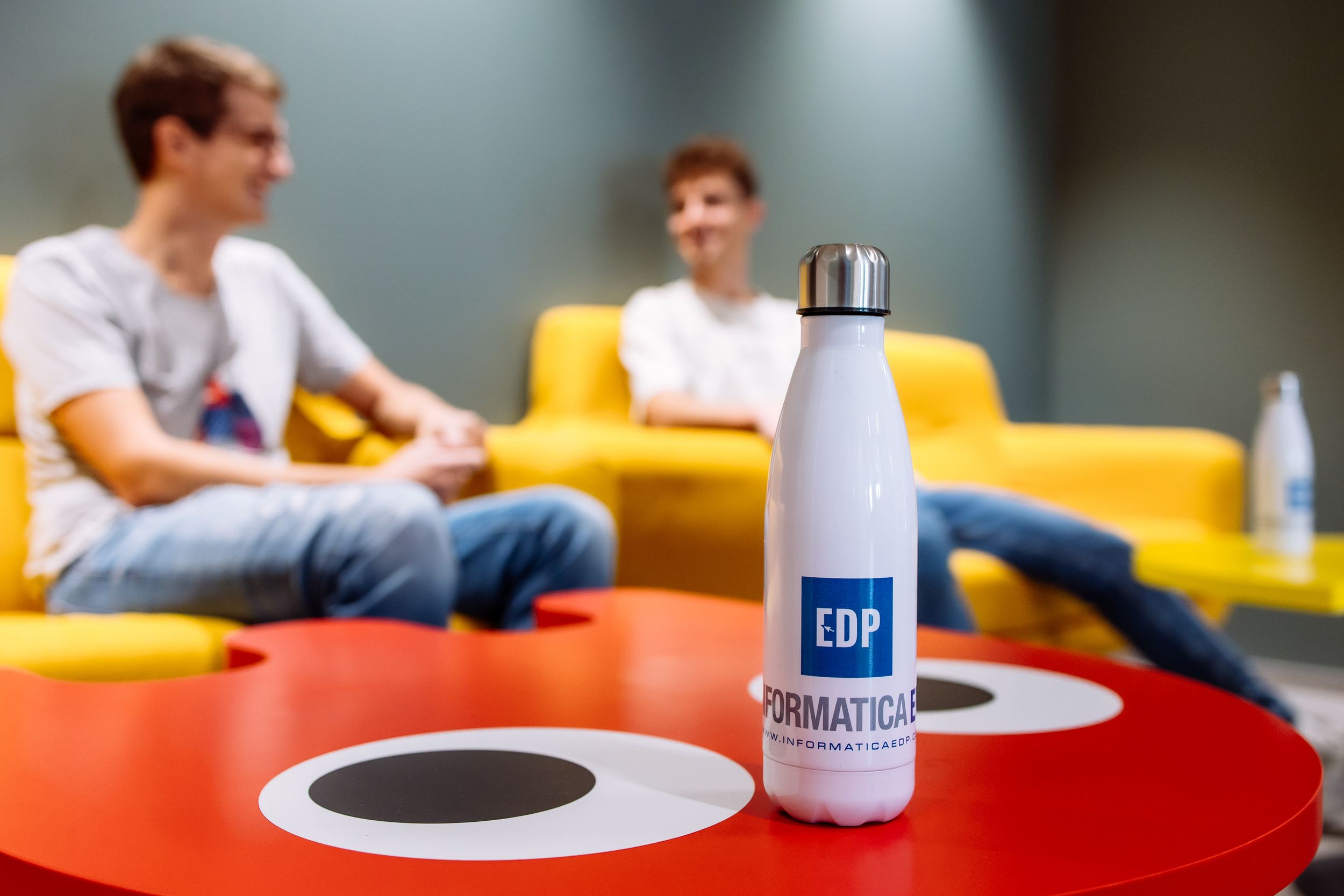 A white water bottle sits on a red table with yellow seating in the background.