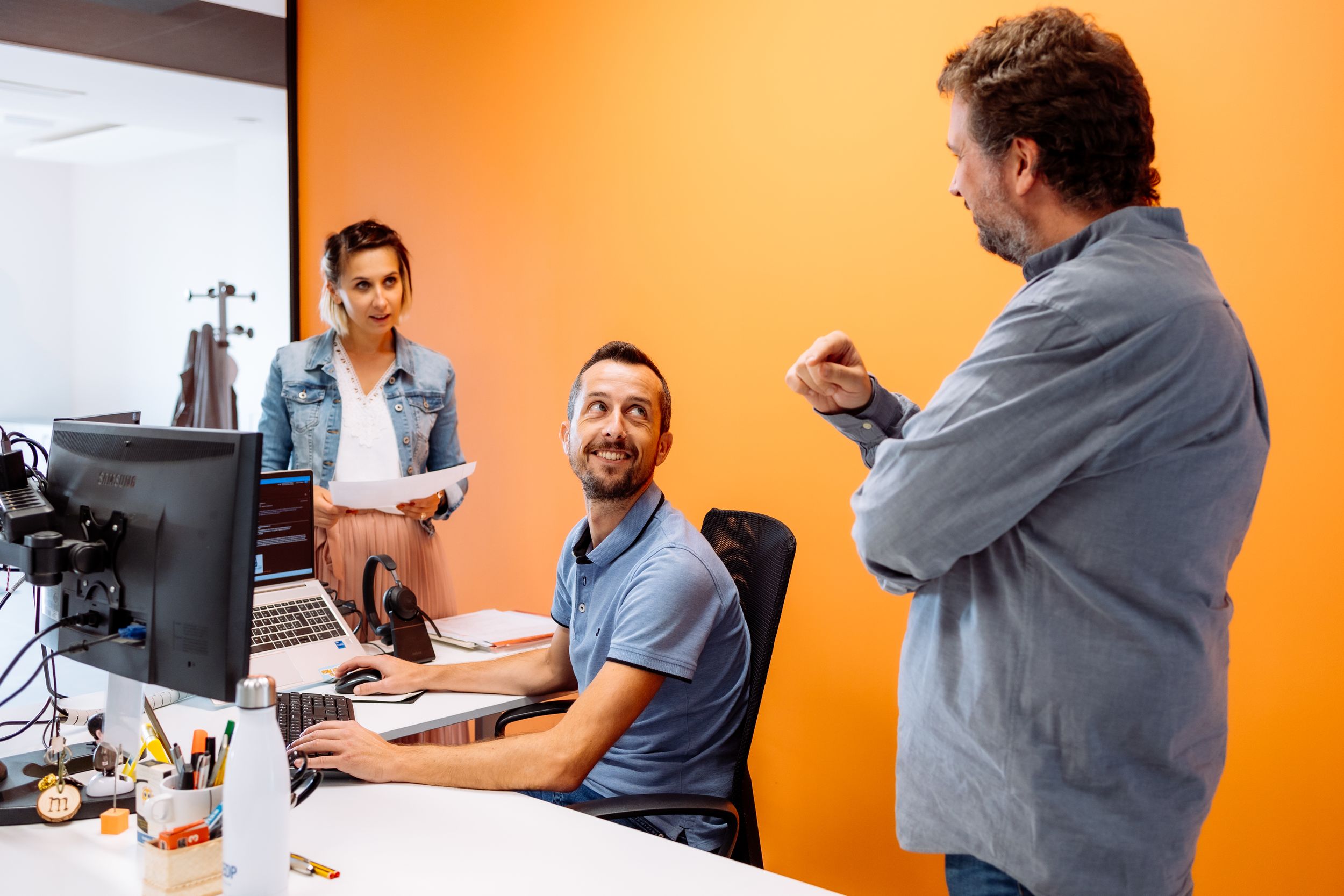 Coworkers having an engaging discussion in a modern office with orange walls.