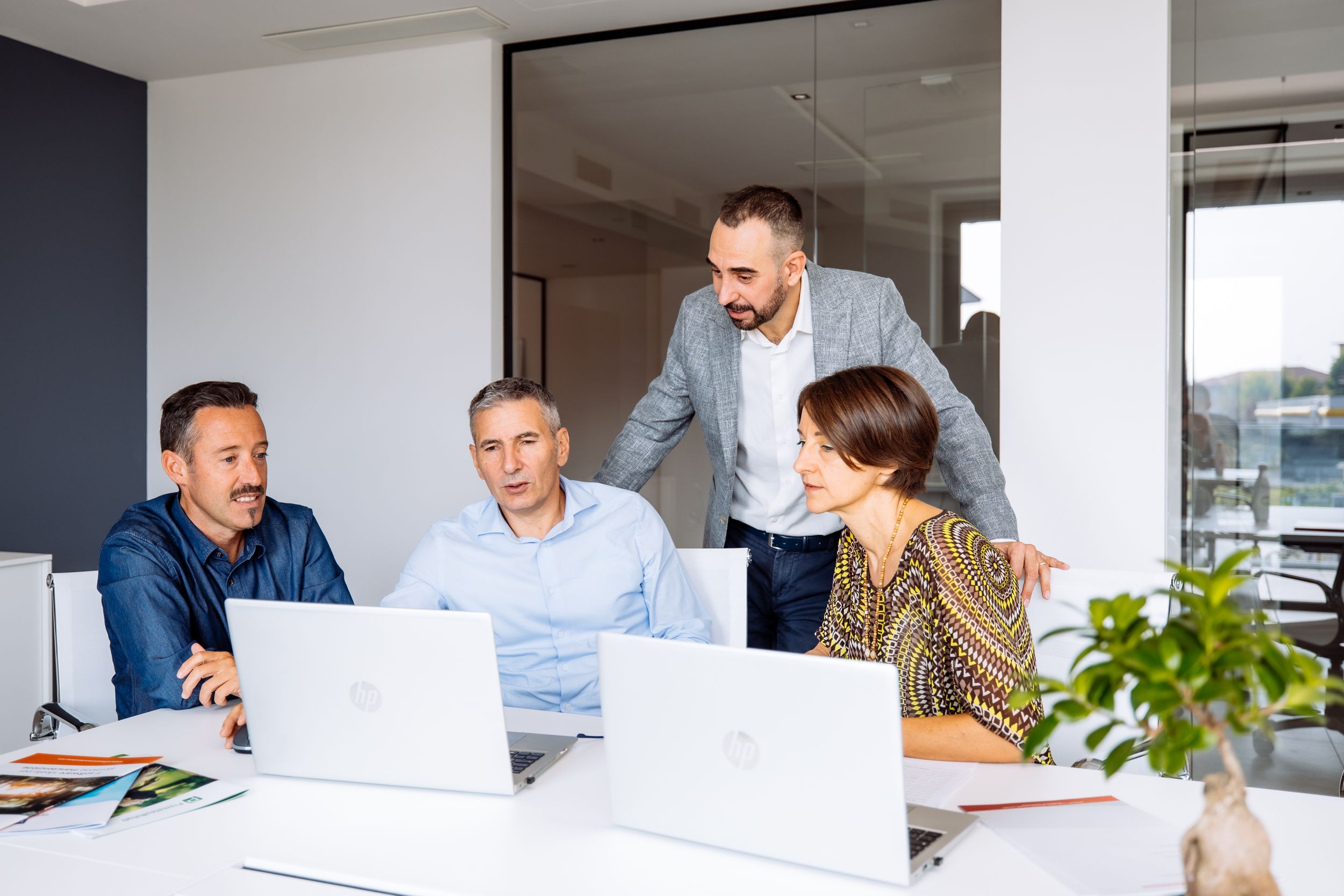 Four business colleagues collaborate around laptops in a modern office meeting space.