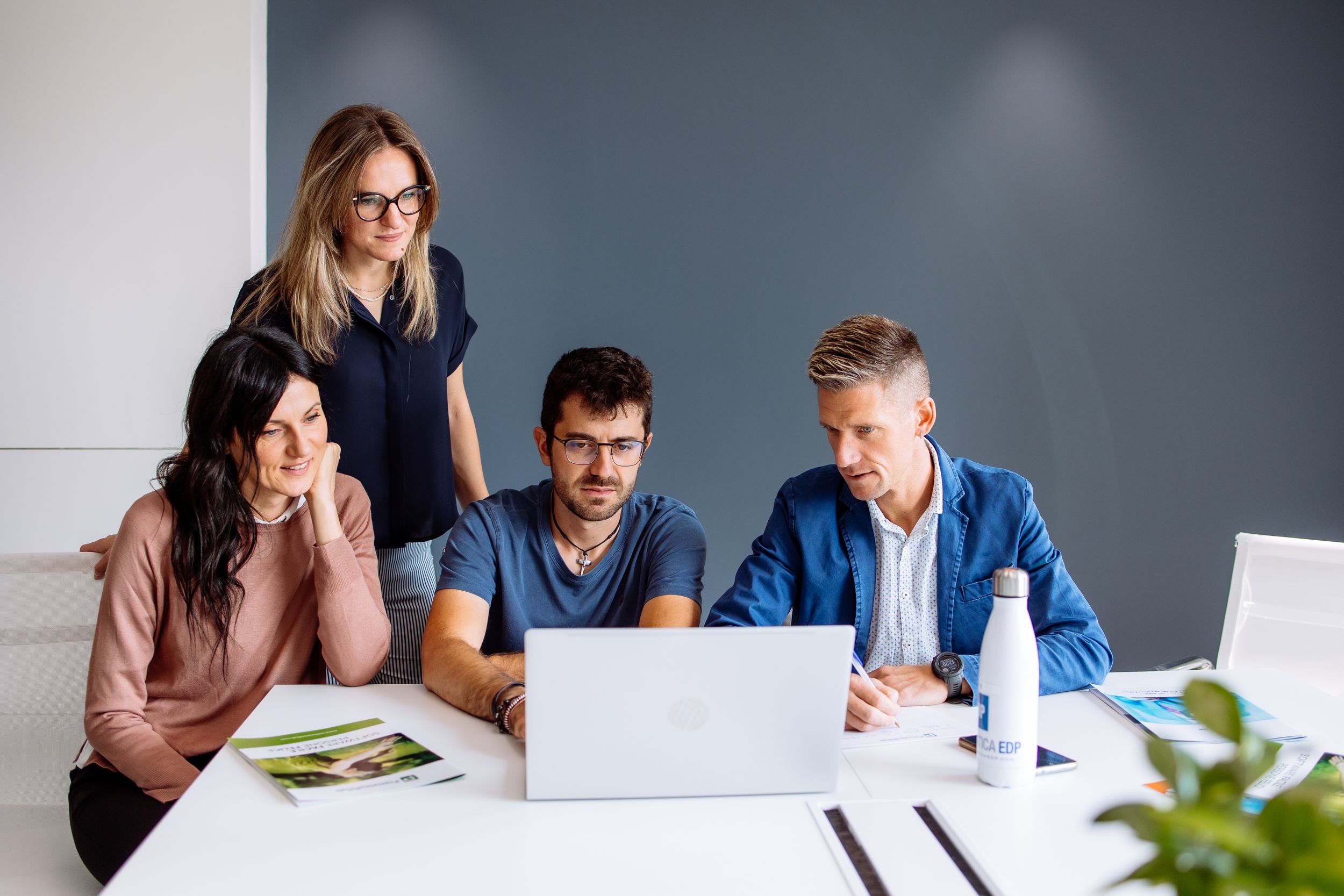 Group of businesspeople collaborating at conference table in modern office space with laptops and paperwork.