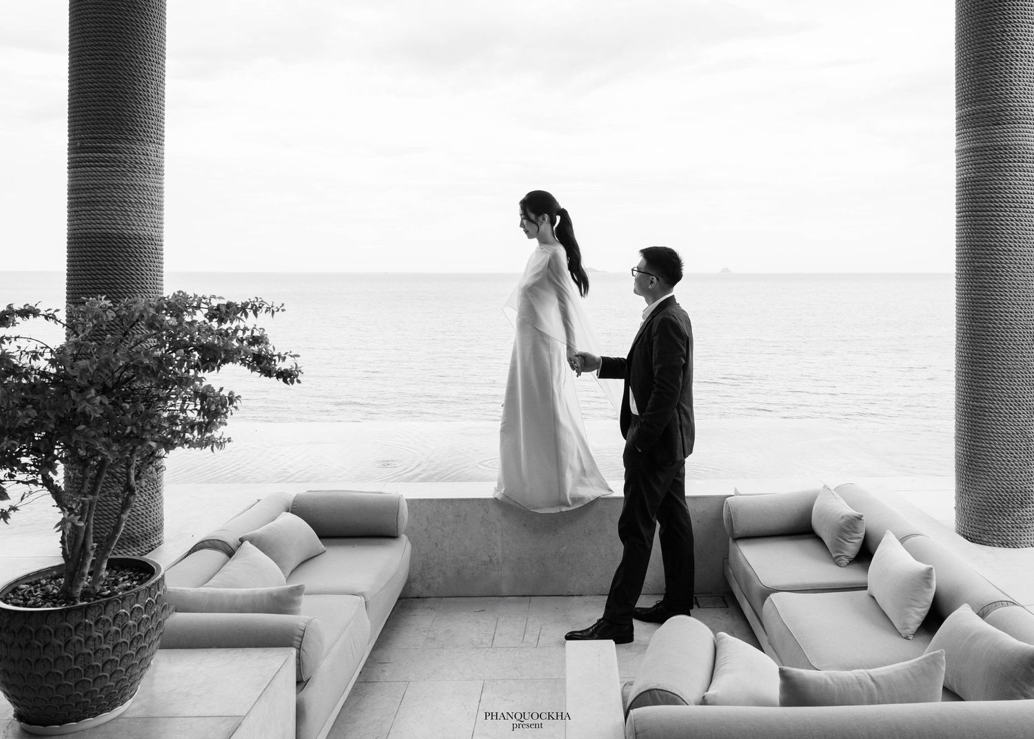 Black and white photo of bride and groom sharing romantic moment on oceanfront terrace.