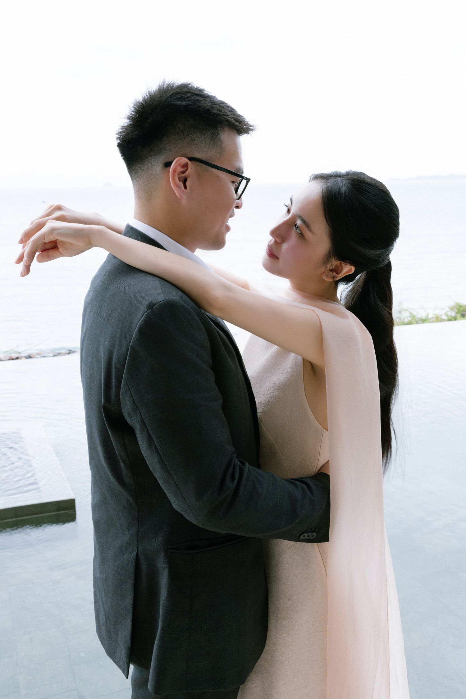Intimate couple embracing and gazing at each other with ocean view in background.
