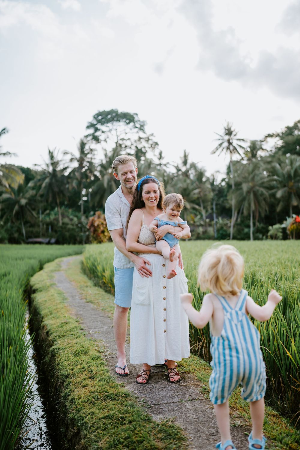Candid family moment captured on pathway between verdant rice paddies during golden hour.