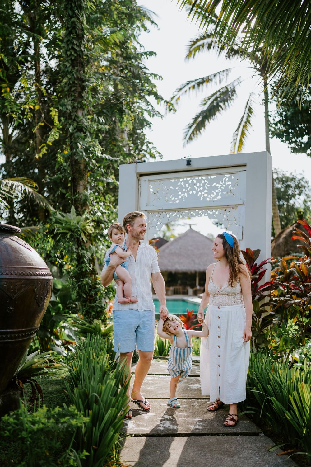 Family walking through a white garden gate surrounded by tropical plants and palm trees.