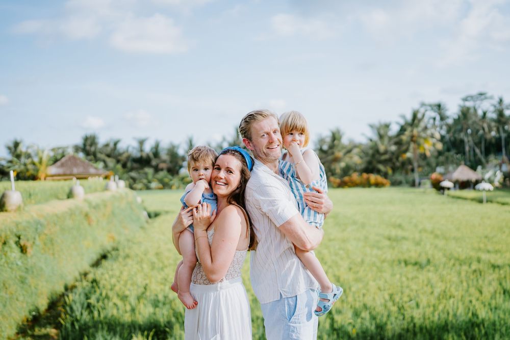 Family photoshoot in an open green field with palm trees in the background.