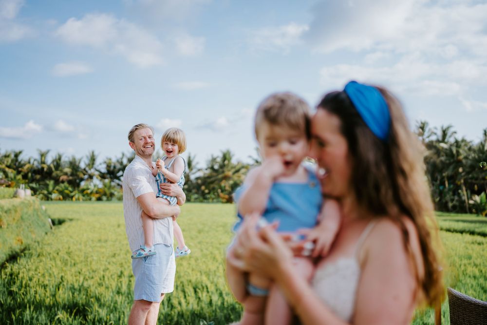 Candid family portraits in a sunny green field with tropical landscape.
