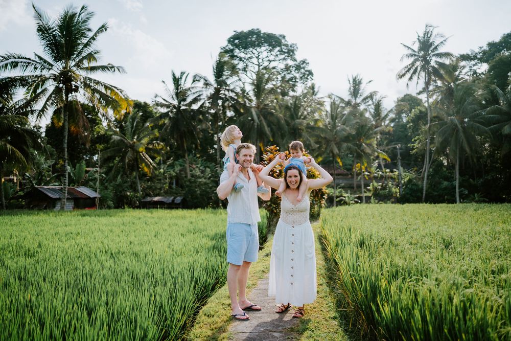 Family walking together on a dirt path through lush green rice fields in Bali at sunset.