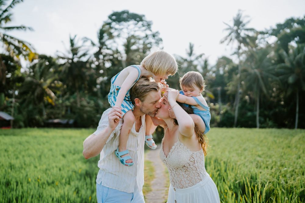 Family photoshoot in a lush green rice field with tropical palm trees in the background.