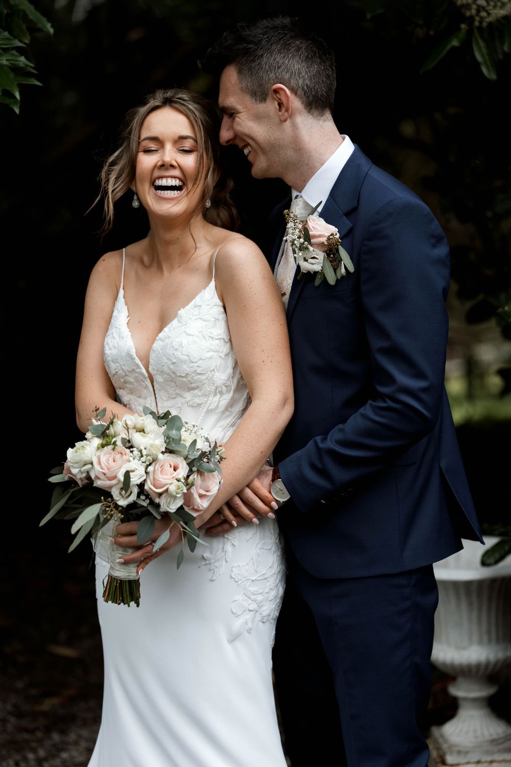 Joyful wedding couple sharing a candid moment with bride holding blush and white bouquet.