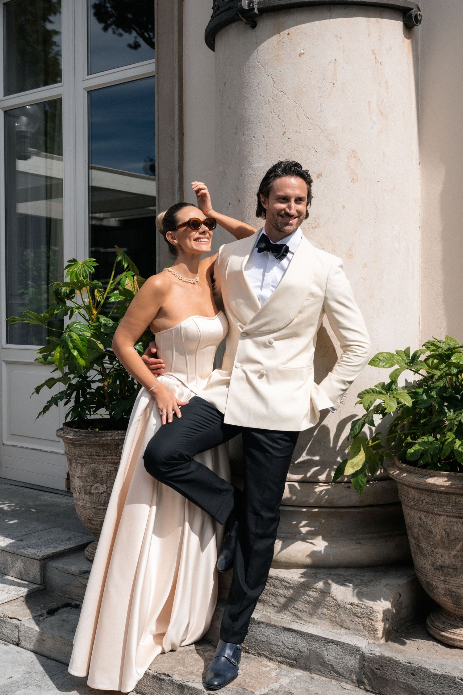 A couple dancing together under elegant stone archways with palm trees visible in the background.