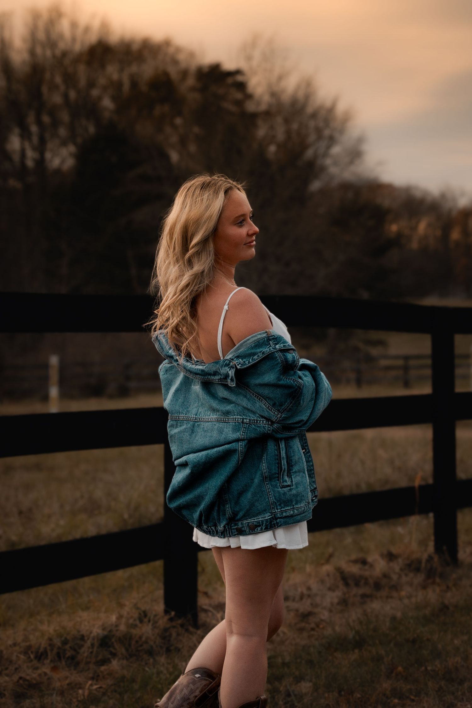 Graduate in denim jacket posing by wooden fence at sunset in Mason Neck, VA | Northern Virginia senior photography.