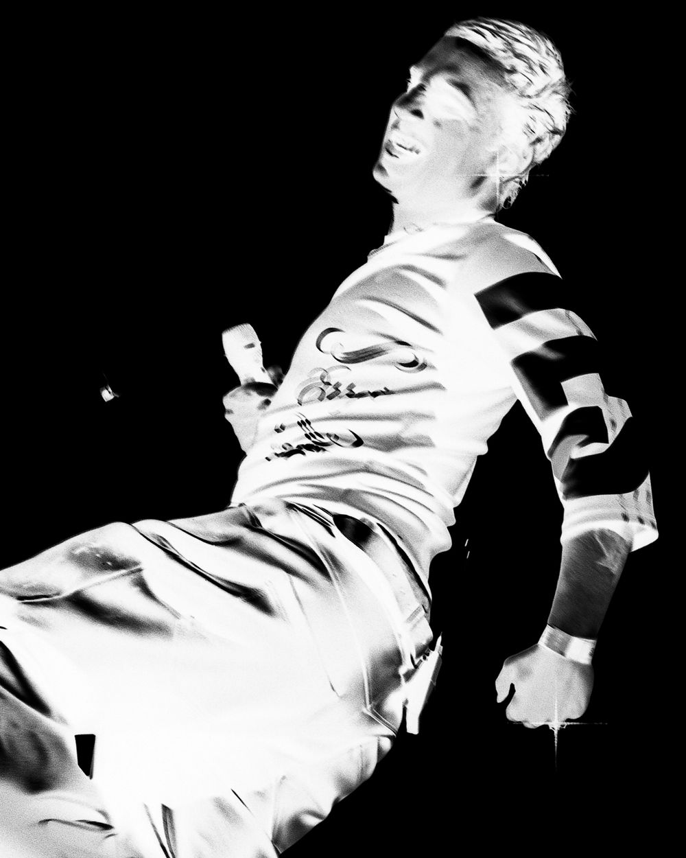 A dramatic black and white sequence showing a person in a light colored jacket moving dynamically against a dark background.