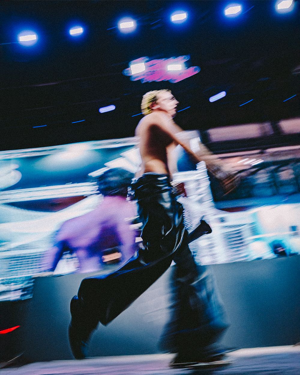 Motion-blurred dancers performing on stage with dynamic blue and pink lighting effects.
