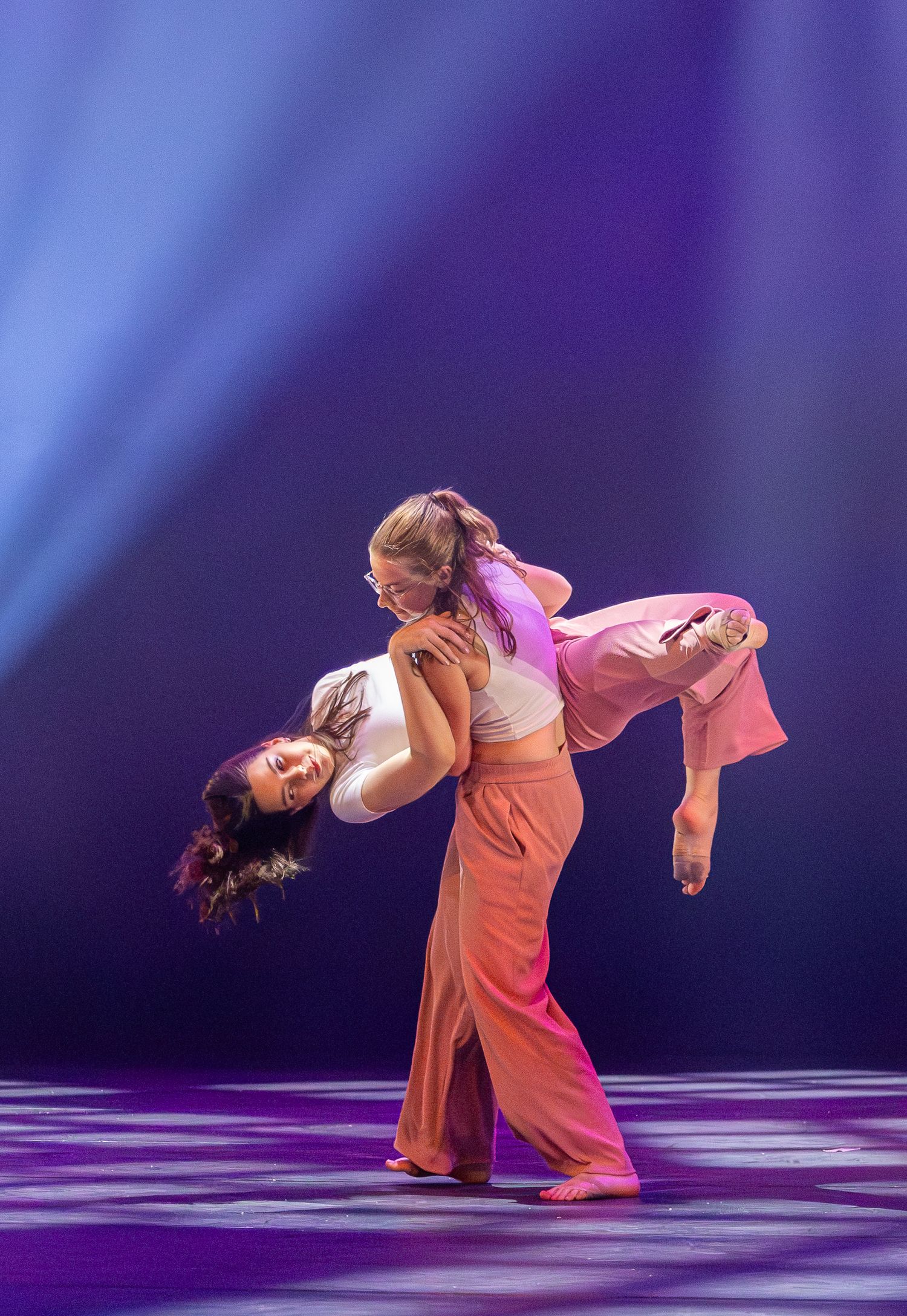 Dancers in white outfits perform a contemporary dance routine on a dark stage with blue lighting.